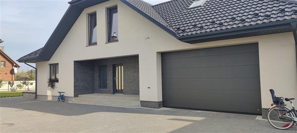 Фото сучасного приватного будинку з автоматичними секційними воротами темного кольору, які забезпечують естетику та функціональність. Ідеальне рішення для гаража.